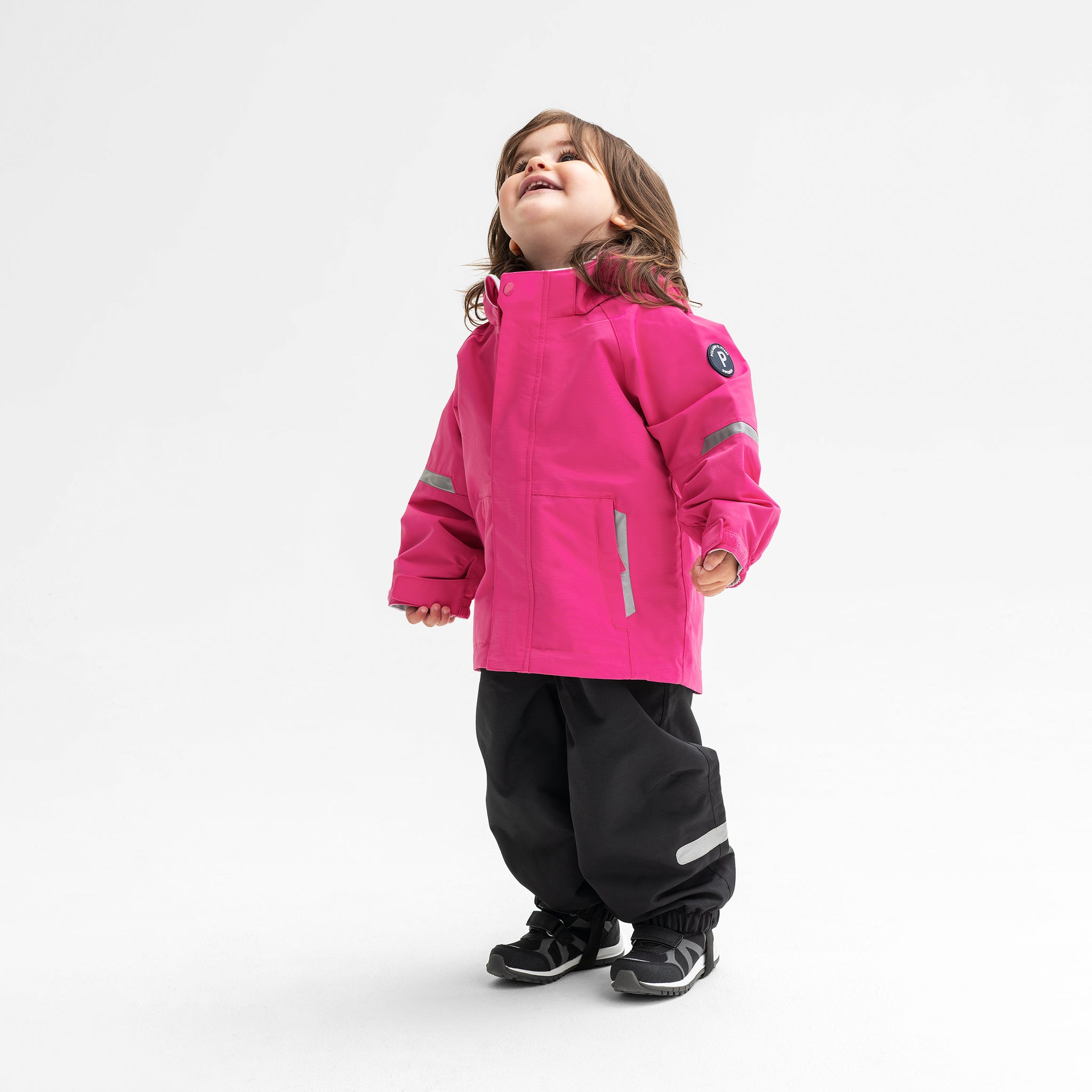 Little girl sporting a pink, kids waterproof jacket, paired with black, kids waterproof trousers, made of shell fabric.